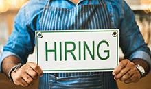 A restaurant worker holding up a hiring sign.