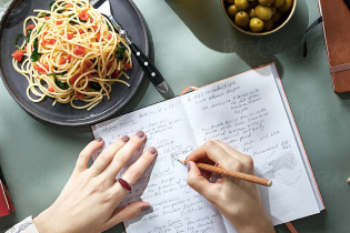 Brainstorming in notebook with a plate of spaghetti and olives