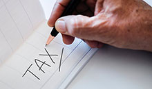 A man writing the word tax in a notebook