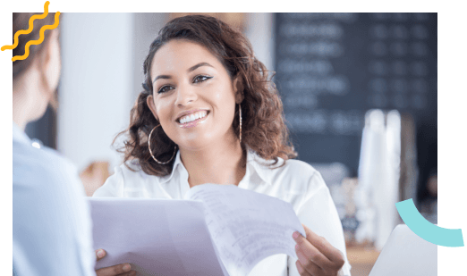 A female restaurant worker smiling while holding papers talking to another woman.