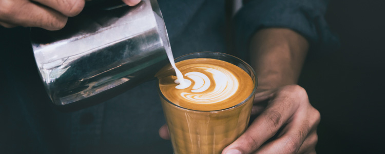 Barista pouring foam into a cup making a design.