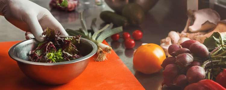 A table of ingredients with a chef placing a bowl of more ingredients on the table.