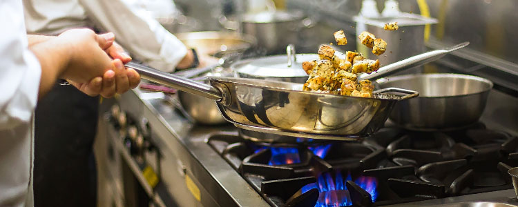 A cook frying chicken on a pan.