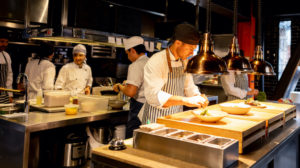 Chef decorating a plate under a hot lamp while working at a commercial kitchen.